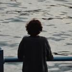 Photography observation practice shown as quiet attention, with a person looking over water in a calm, unforced moment.