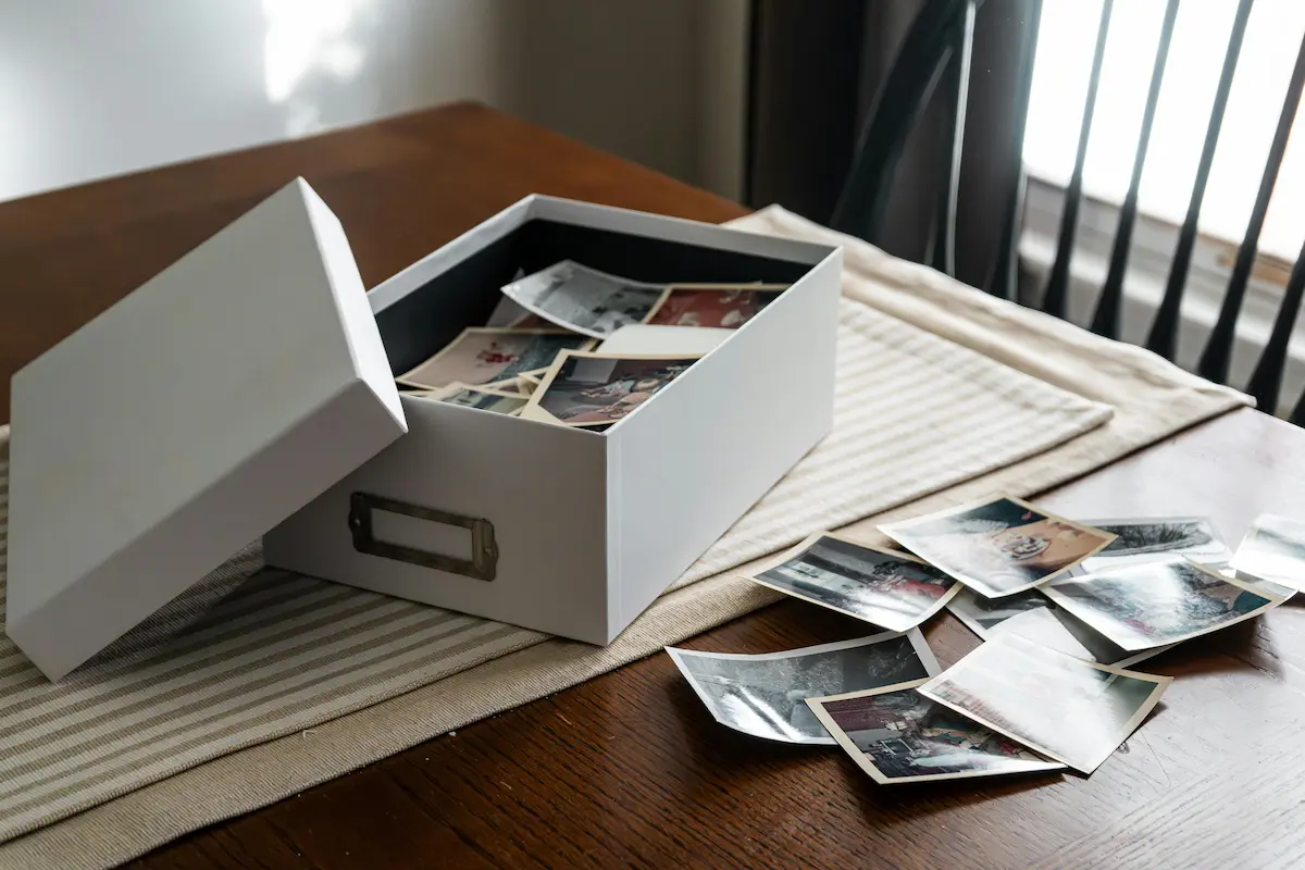 Photography workflow example: a photo archive box with printed photographs spread across a wooden table in soft window light.